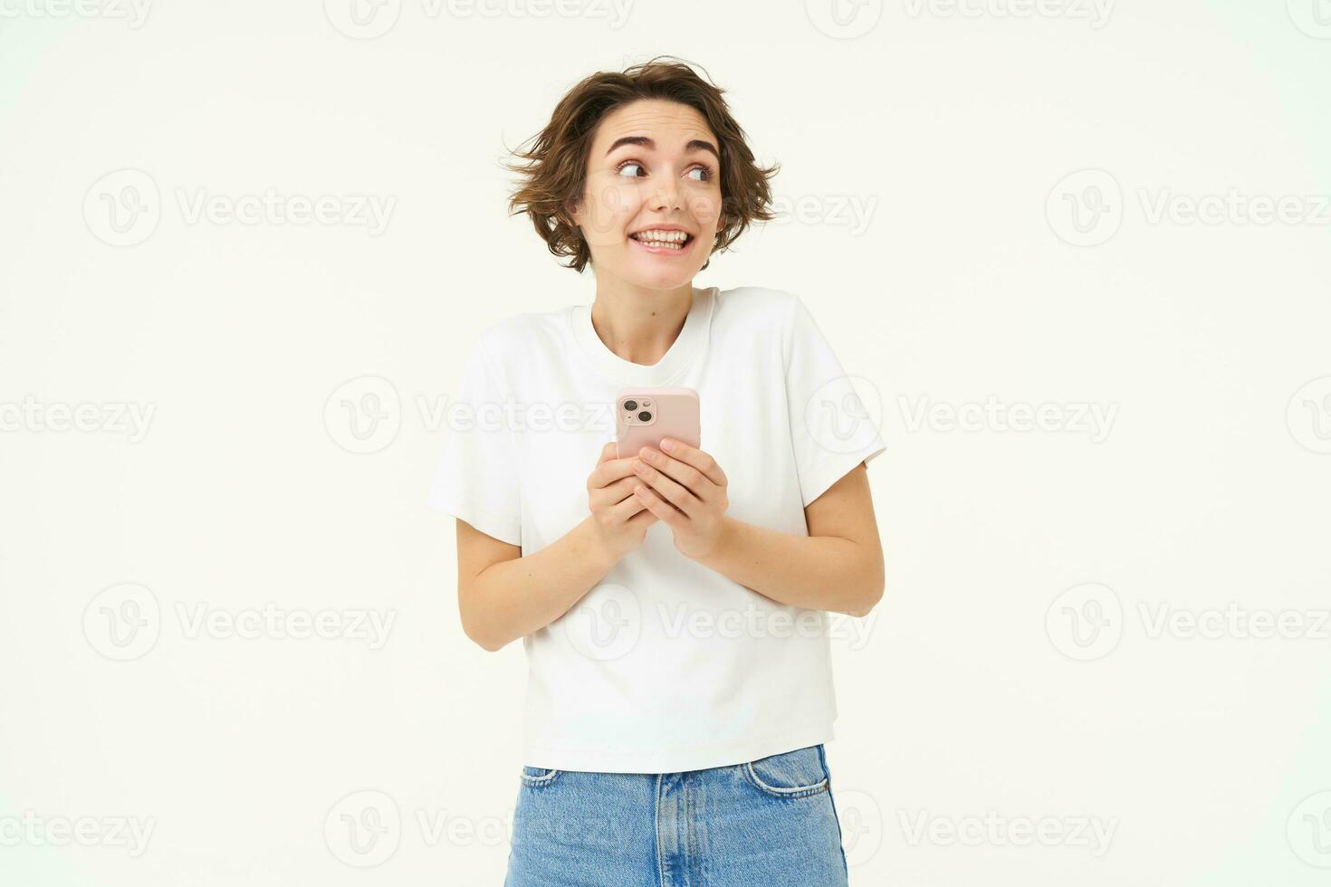 retrato de morena niña con teléfono inteligente, enviando un mensaje, utilizando móvil teléfono solicitud, sonriente y mirando feliz, blanco estudio antecedentes foto