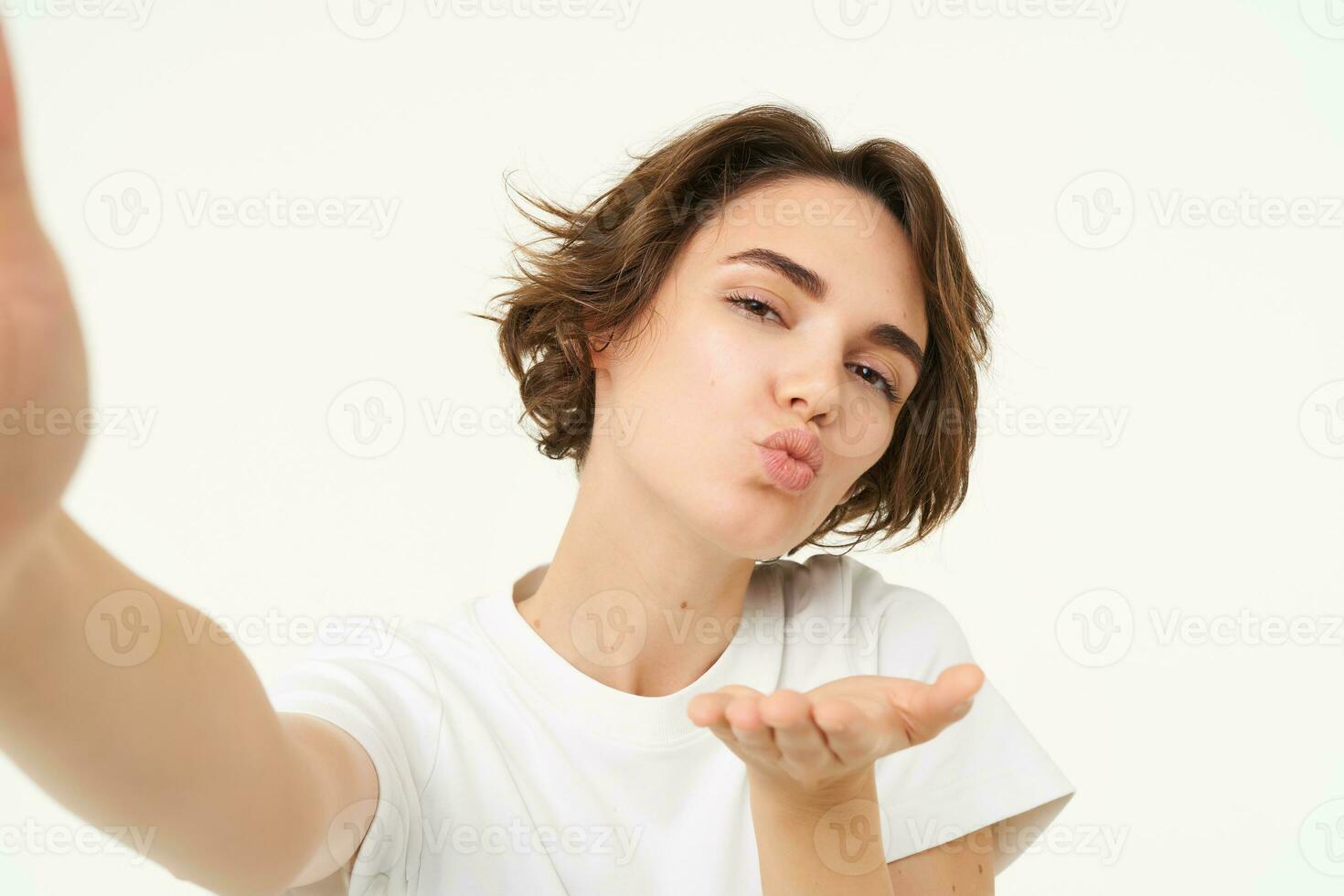 Close up of smiling brunette woman makes selfie, taking photo for her social media, holds mobile phone with extended hand, standing over white background