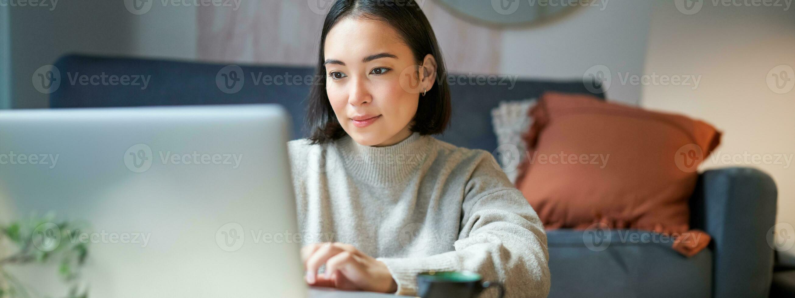 Self employed young korean woman working on remote, typing on laptop, studying at home in living room photo