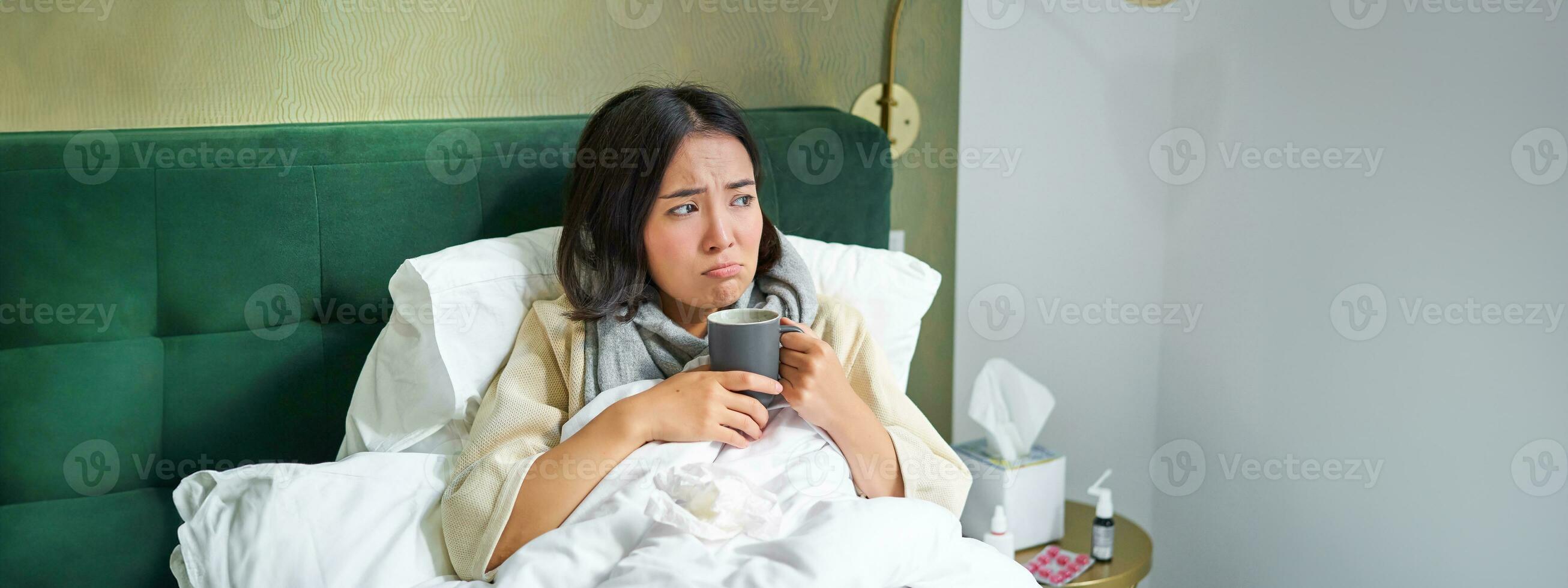 Flu, sickness and people. Young woman feeling sick, having fever and catching col, lying in bed with hot tea, taking drugs from influenza photo