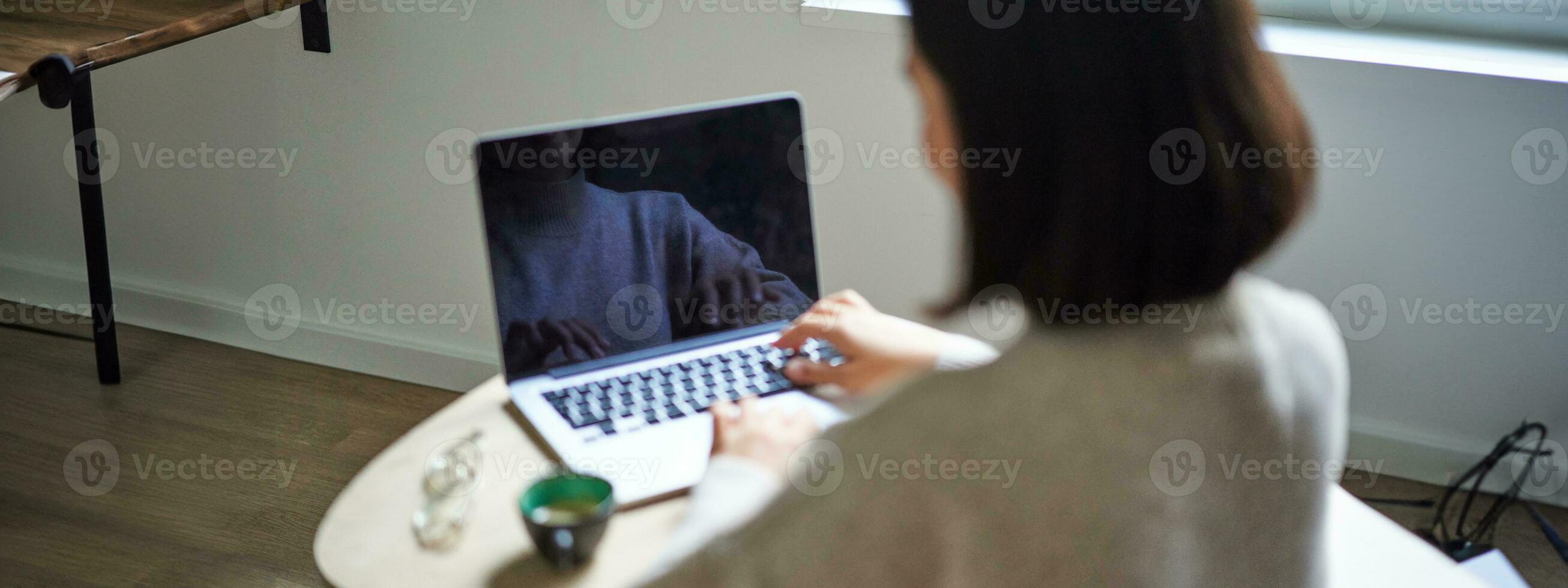 Rear view of woman, typing and working on laptop, computer screen is empty for copy space, female student studying remotely photo