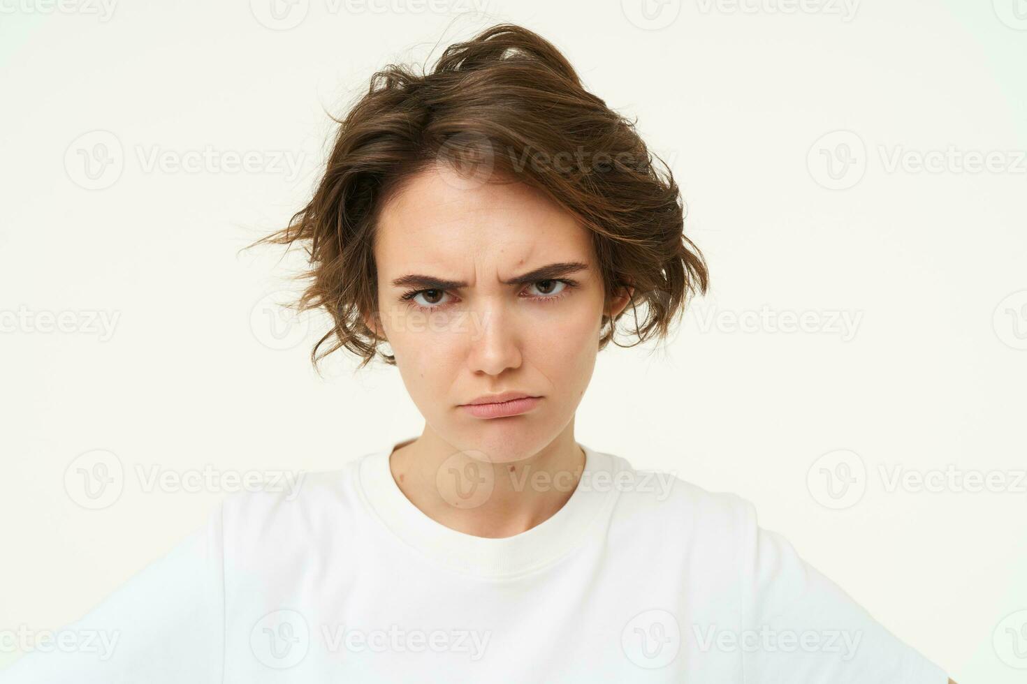 Close up of brunette woman shows angry face, frowning grumpy, pouting and looking disappointed, standing over white background photo