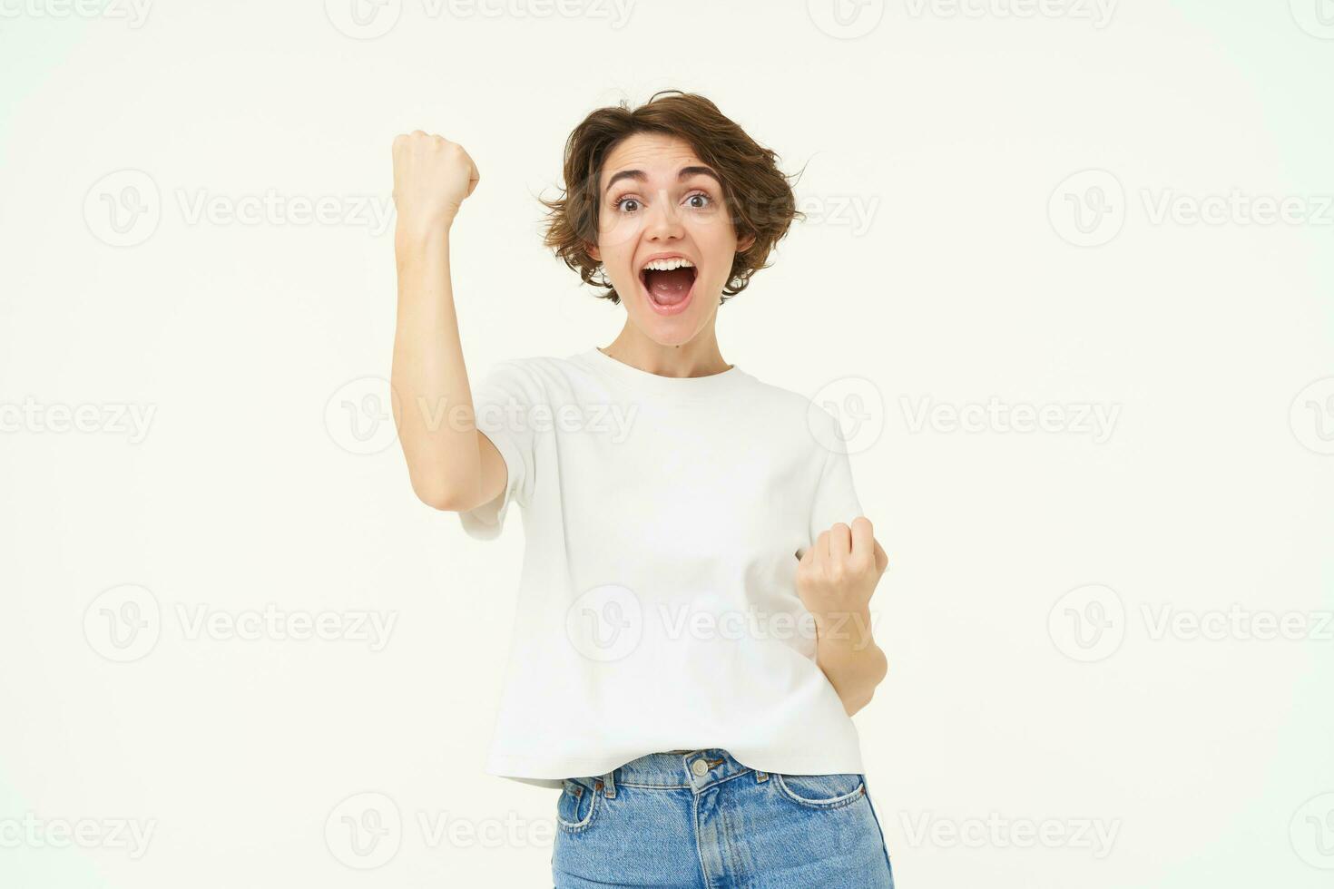 emocionado morena chica, estudiante victorioso premio, celebrando victoria, triunfando, en pie en blanco camiseta y pantalones terminado blanco antecedentes foto
