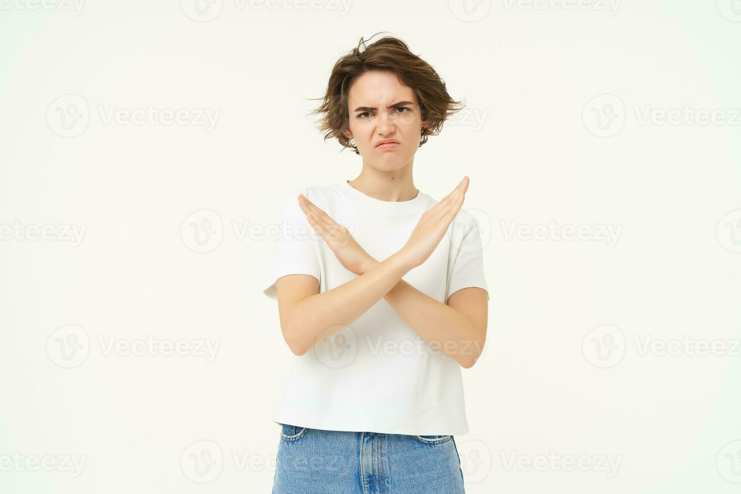 Portrait of woman with serious face, shows cross, stop gesture, prohibit something bad, standing over white background photo
