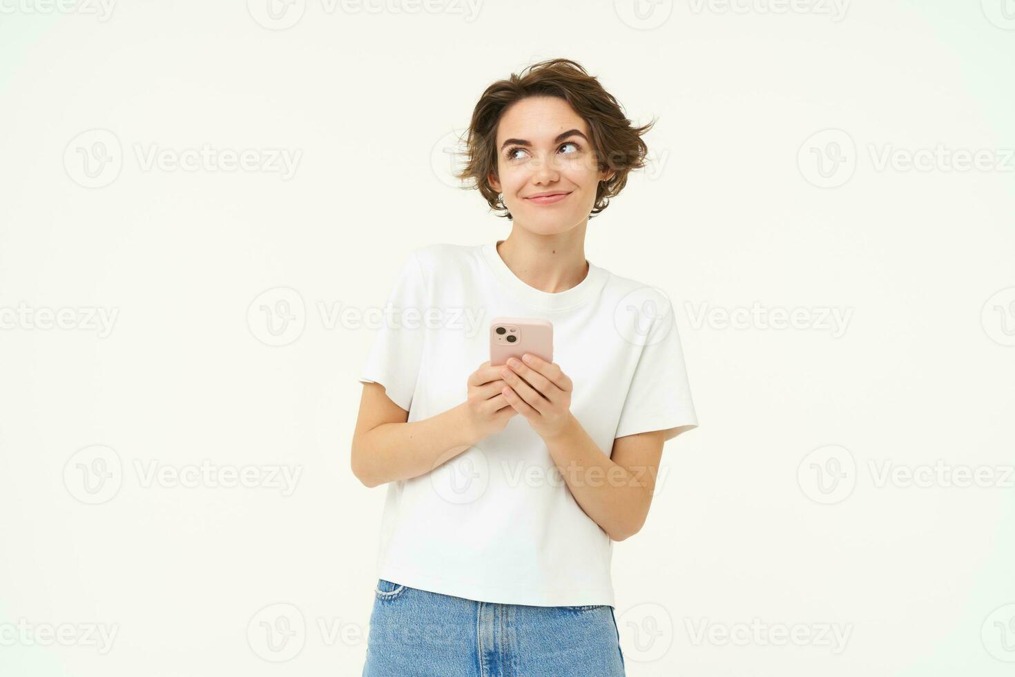 Portrait of cute modern woman with mobile phone, smiling, using smartphone app, doing online shopping on application, standing against white background photo