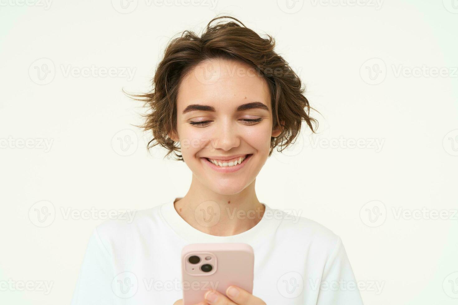 Close up portrait of young woman smiling, using smartphone, texting, checking her mobile apps, stands over white background photo