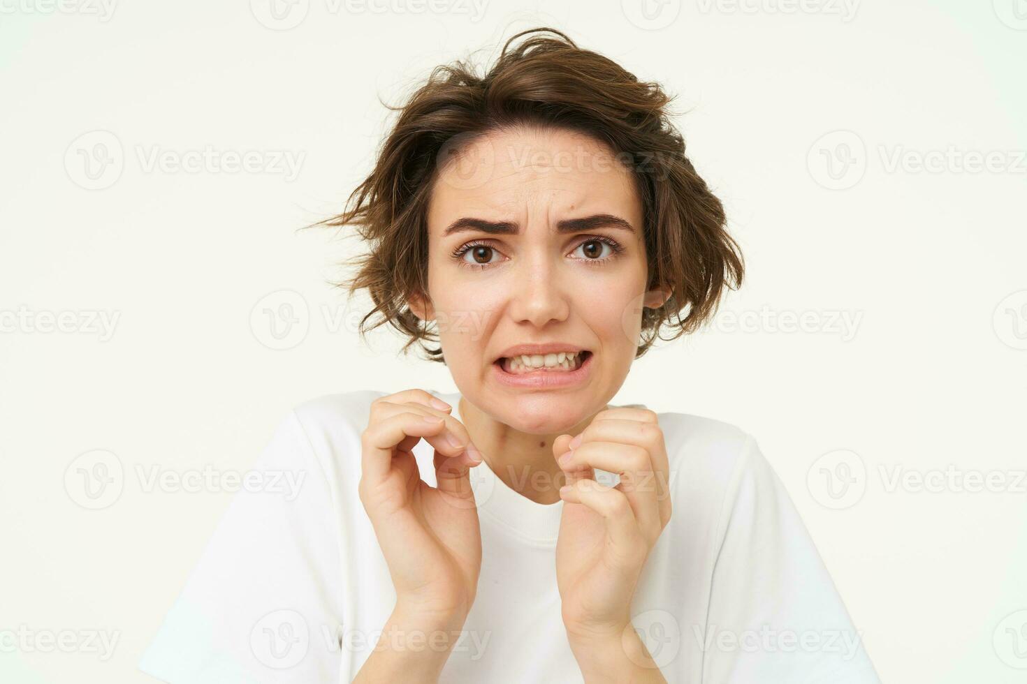 Close up portrait of woman cringing, looking disgusted, jumps from fear and looks afraid, stands over white background photo