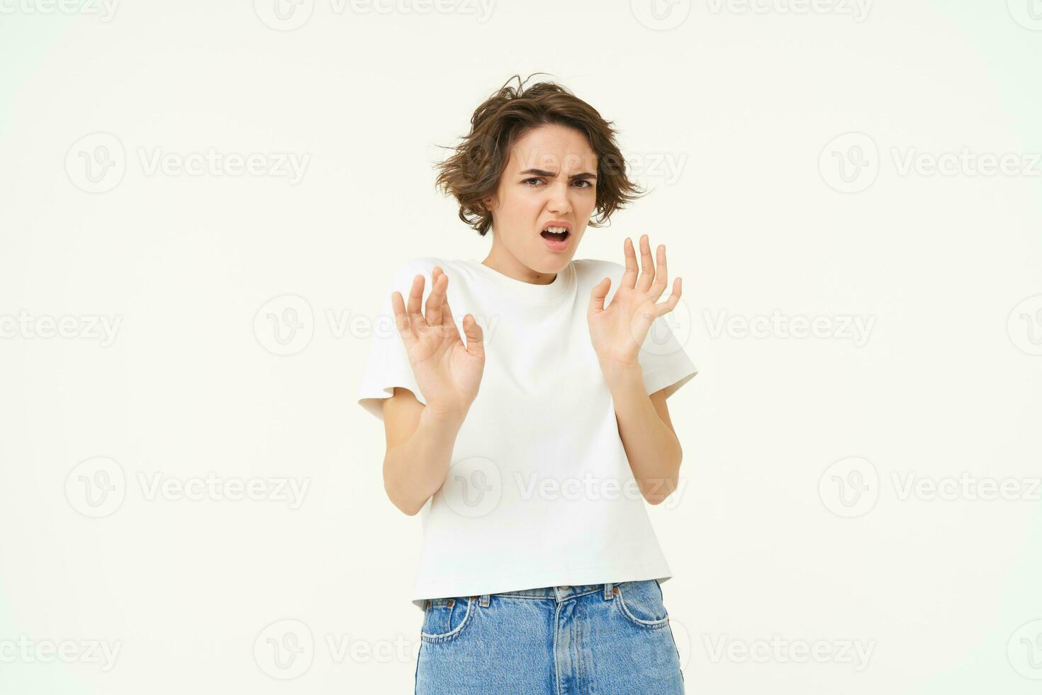 Young woman raises hands up and refuses, rejects smth, tried to block something disgusting, standing over white background photo