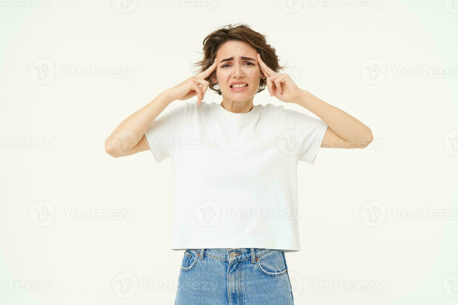 Image of distressed, upset young woman touches her head, has headache, suffers from migraine, stands over white background photo