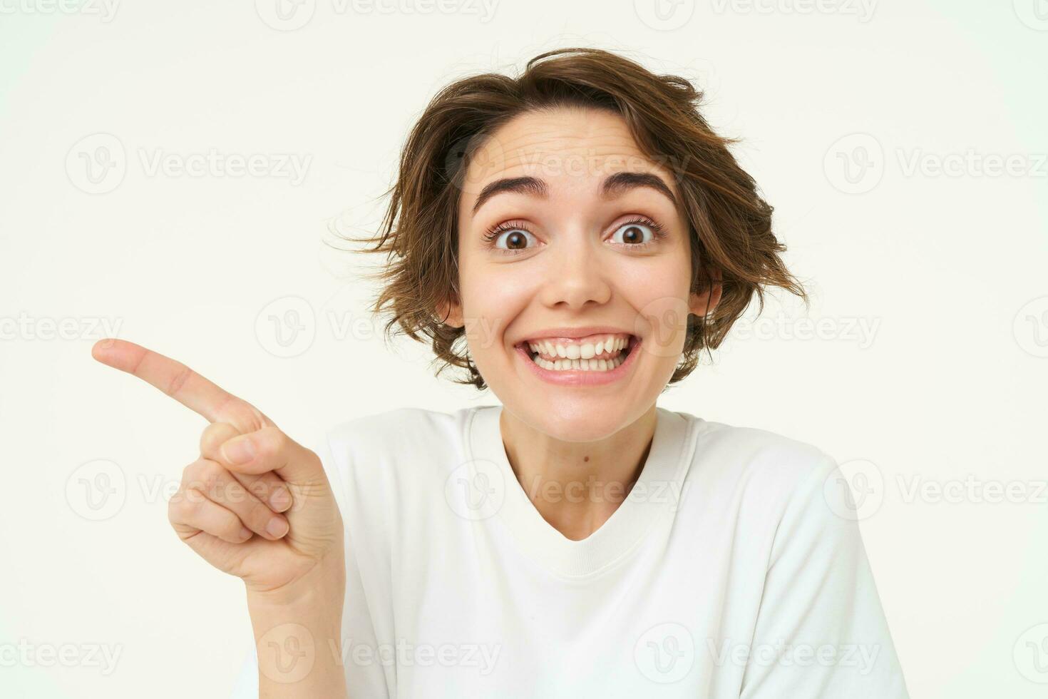 Image of candid brunette girl, pointing left, showing advertisement, recommending store, standing over white background photo