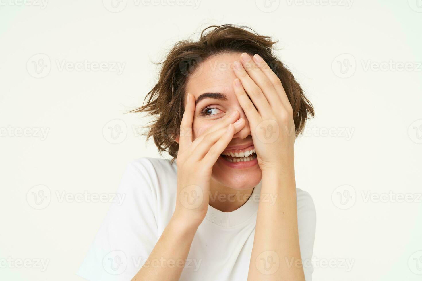 Image of funny woman peeking through fingers, looking at something with curious face expression, waiting for surprise and smiling excited, isolated over white background photo