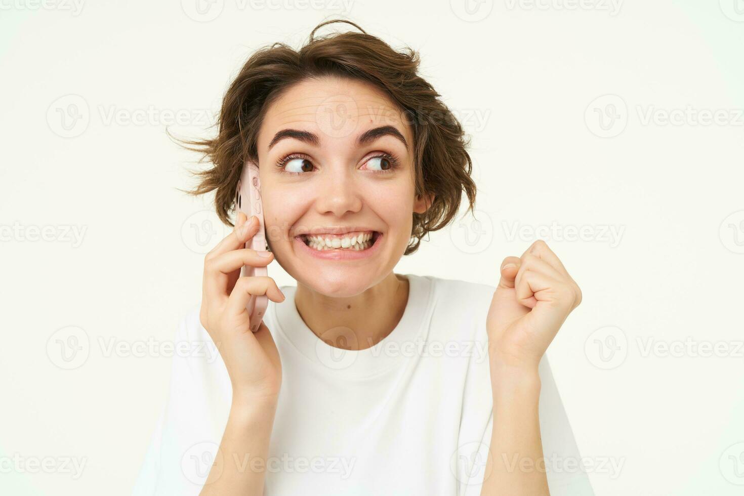 Image of cute brunette woman answer phone call, talking on smartphone, holding mobile near eat and smiling , standing over white background photo