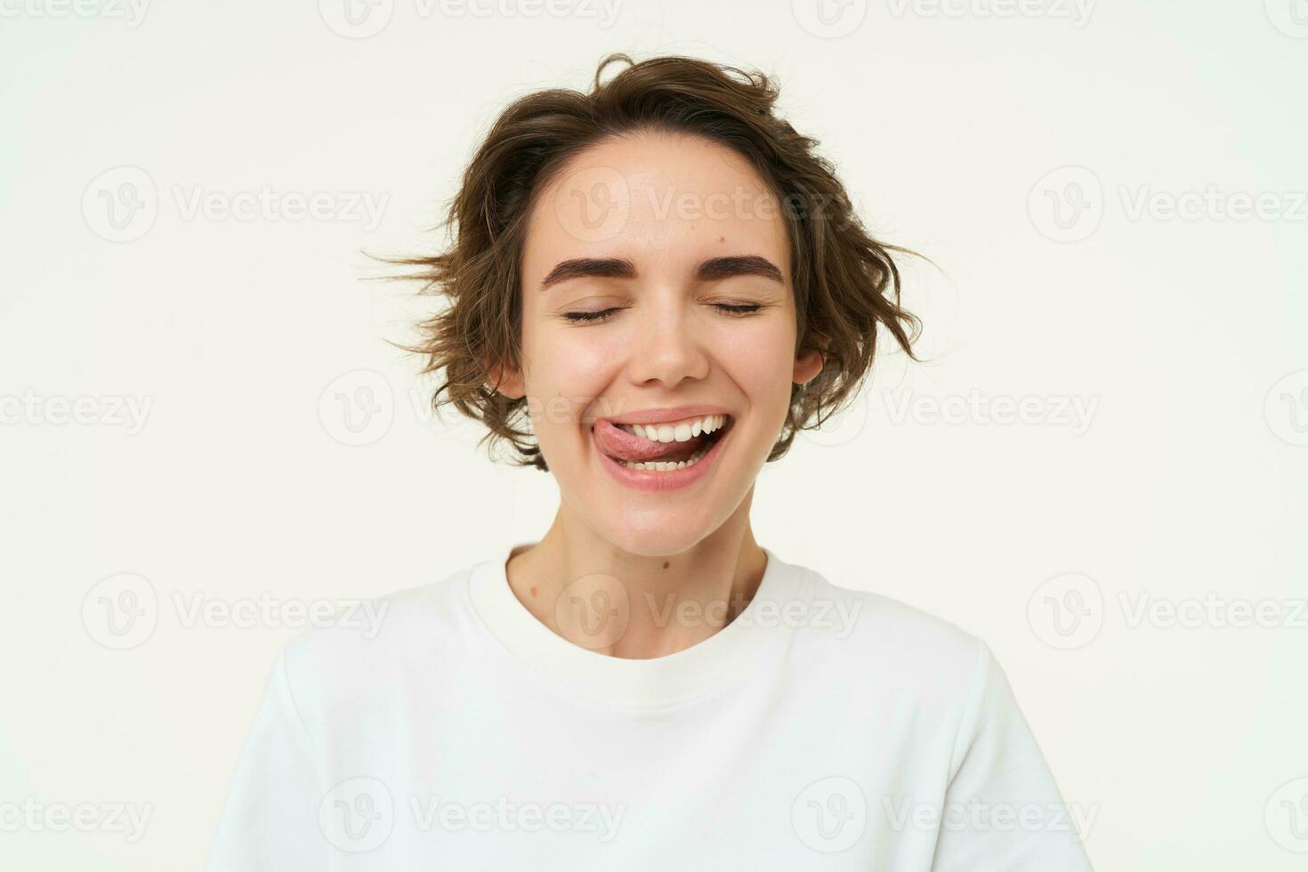 Close up of happy smiling woman, licks her white teeth, feels happy after dental treatment, isolated against studio background photo