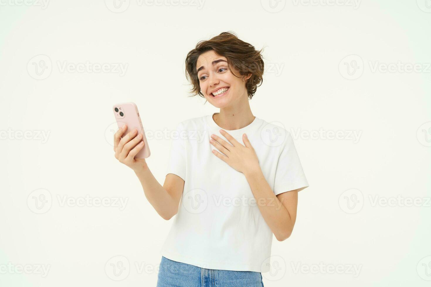 Portrait of girl talking on mobile phone, video chats with friends on smartphone, standing over white studio background photo