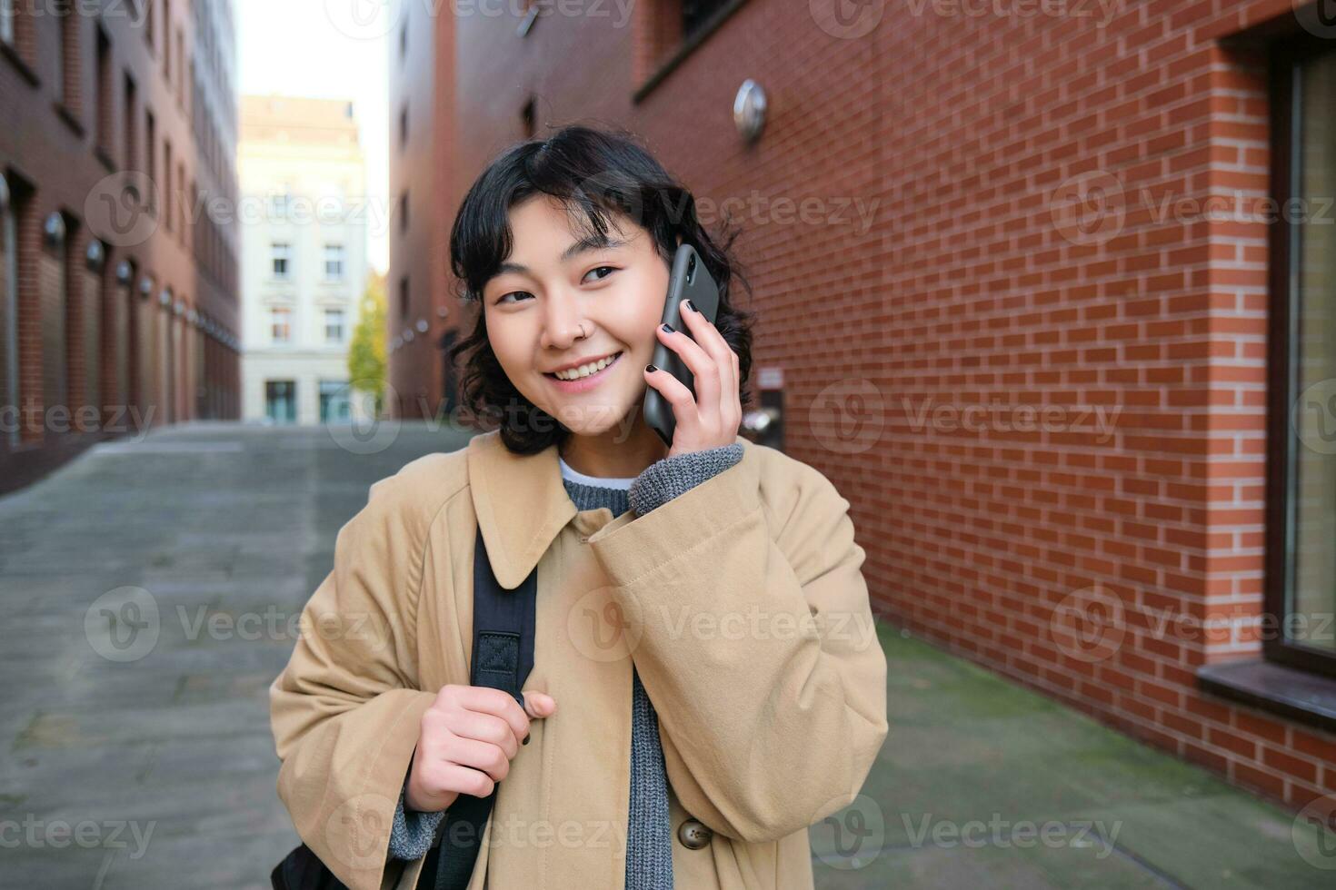 celular tecnología concepto. joven moderno niña negociaciones en móvil teléfono, camina en calle y sonrisas, tiene conversacion terminado teléfono foto