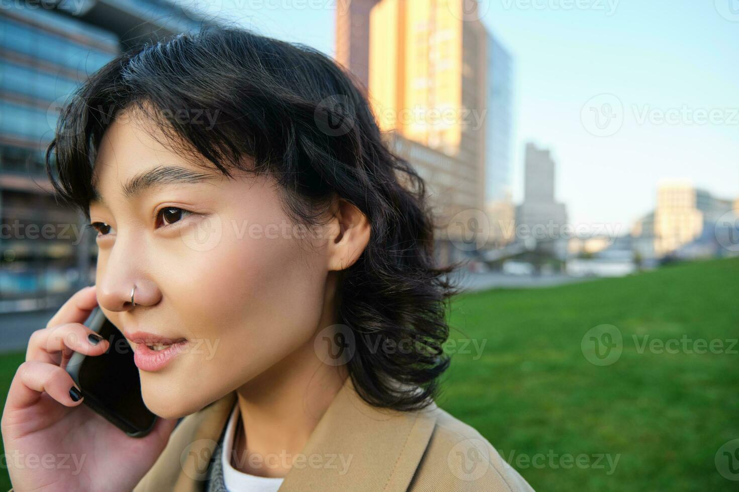 Headshot of young korean woman walks on street, talks on mobile phone, has telephone conversation, stands near campus building photo