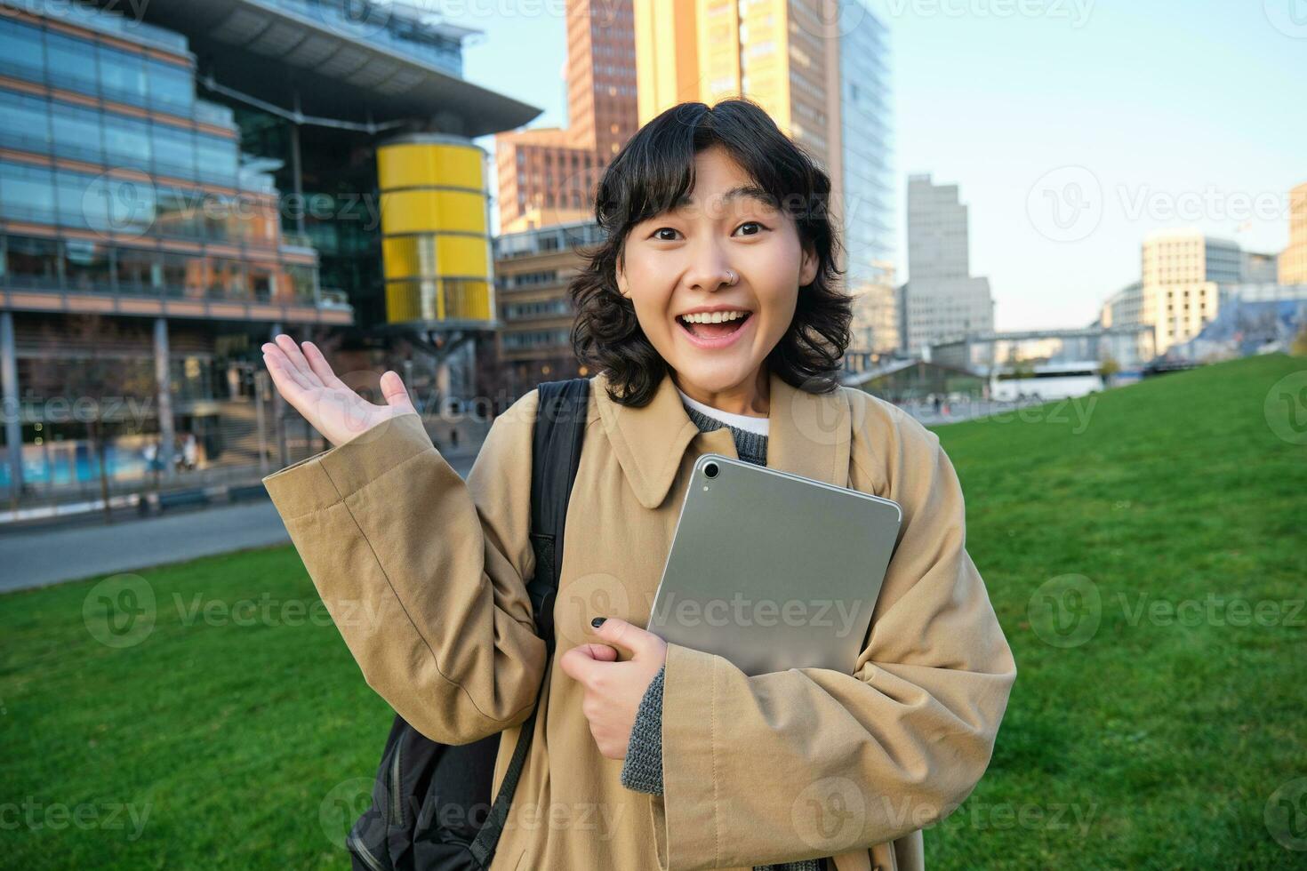 entusiasta morena asiático chica, estudiante con digital tableta en su manos, mira impresionado y sorprendido, miradas a cámara con asombro, soportes en calle en temor foto