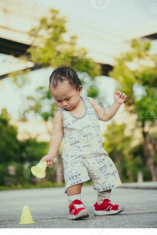 Little toddler boy is playing with yellow cone marker. Child is standing holding marker practice cone. 1 year old son is playing on playground outside the house. Vertical photos. photo