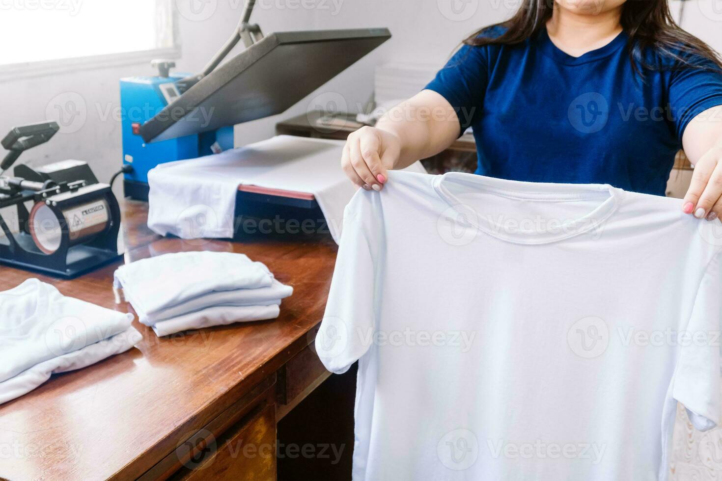 unrecognizable woman, holding white shirts behind a sublimation or screen printing machine for t-shirts. photo