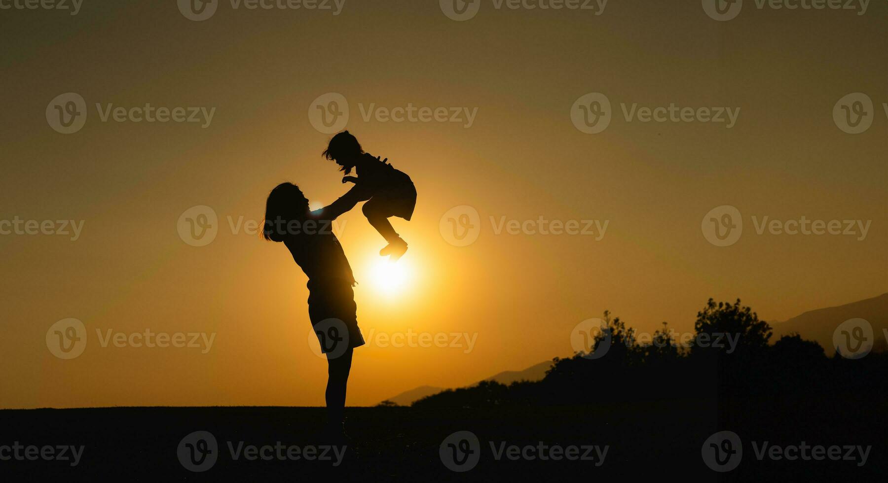 silueta, contento madre y hija abrazo lanzar alto en el campo césped a puesta de sol en el noche. amor familia actividad relajarse concepto. foto