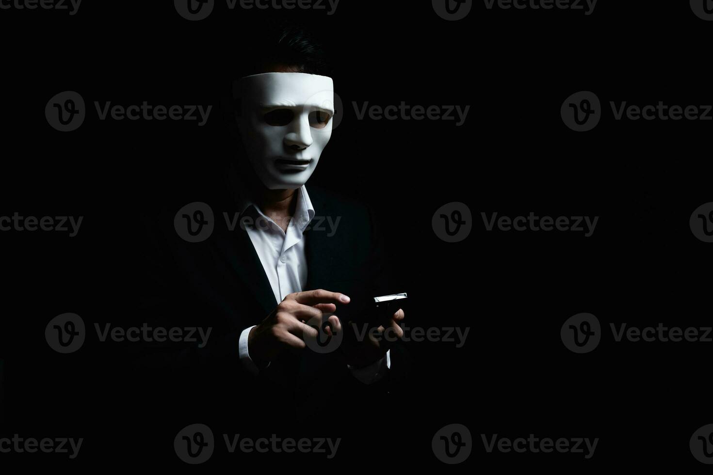 Unknown businessman wearing mask with covered face using mobile phone makes an anonymous call intimidating and threatening the interlocutor on dark background. hacker callcenter concept. photo