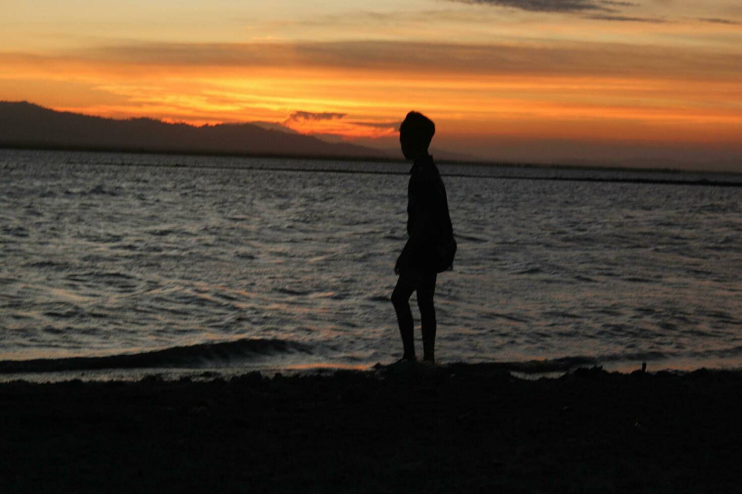 Silhouette of a young man standing by the lake enjoying the sunset. peaceful atmosphere in nature photo