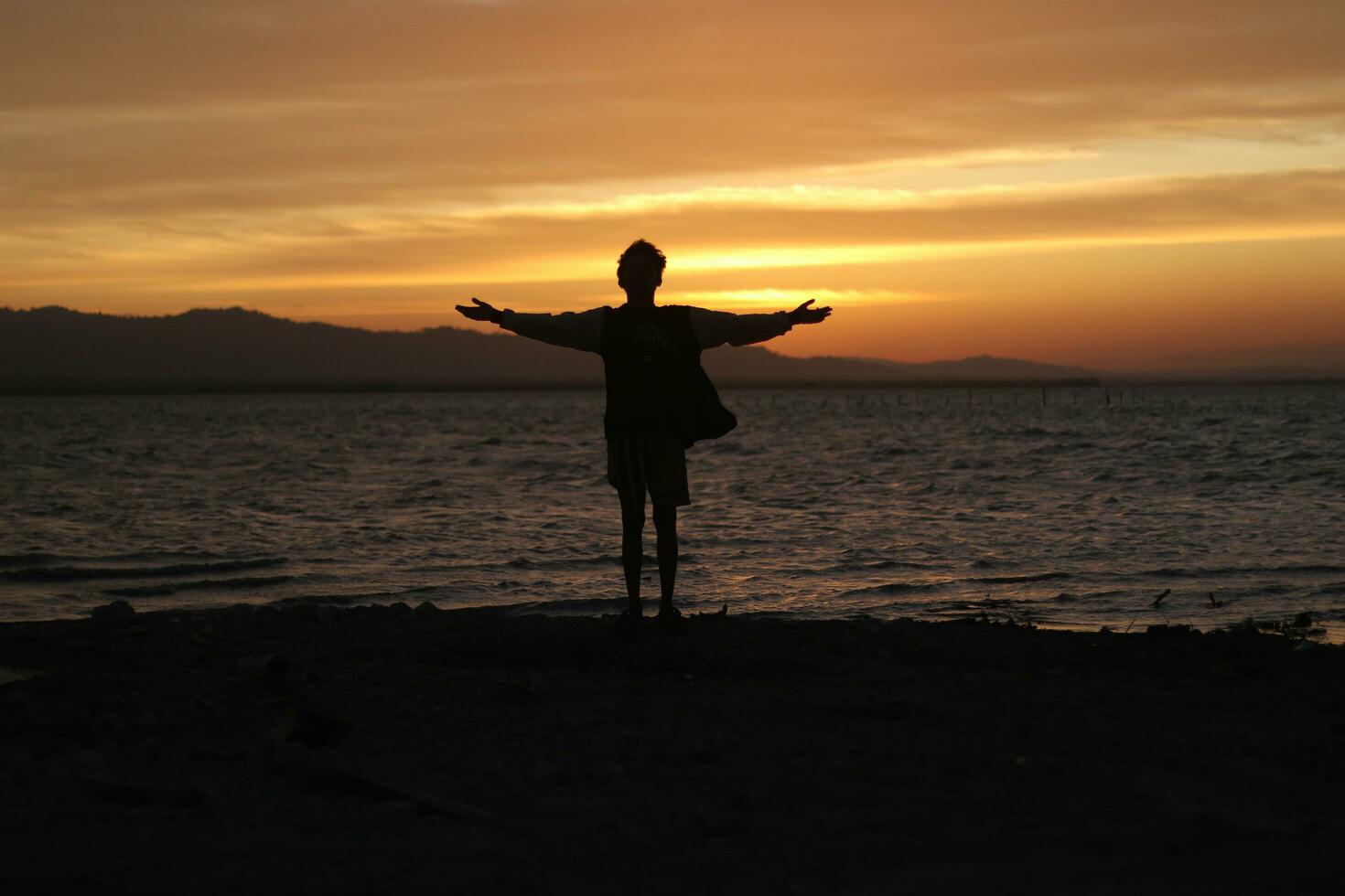 Silhouette of a young man standing by the lake enjoying the sunset. peaceful atmosphere in nature photo