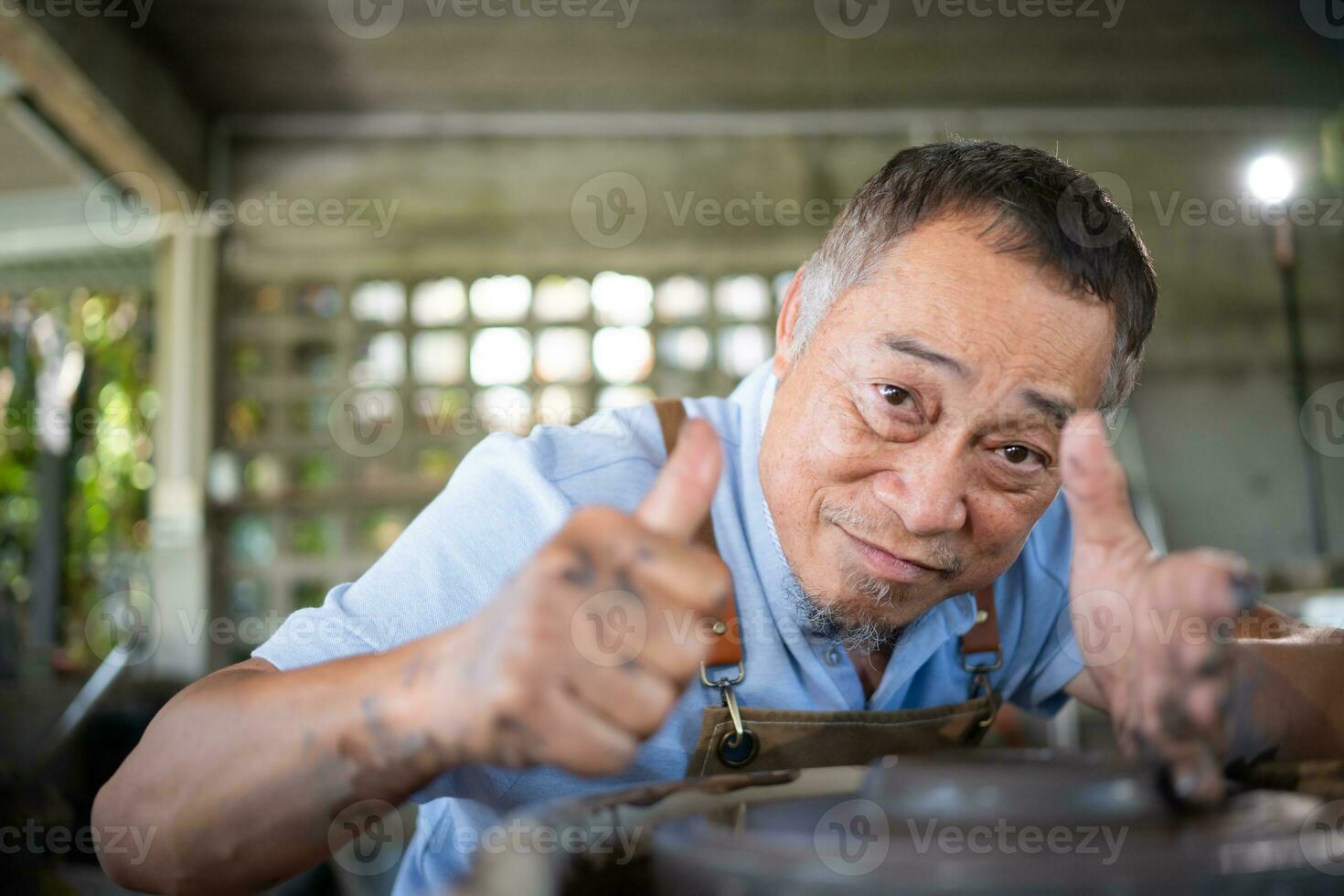 Portrait of senior craftsman working on pottery with thumb up photo