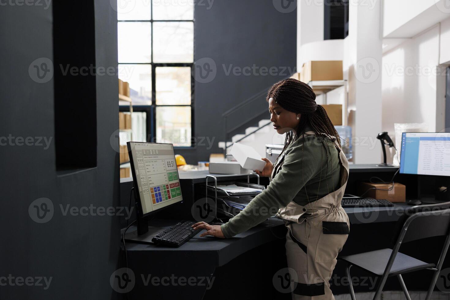 Warehouse employee looking at carton white boxes, checking shipping details on computer in storage room. African american supervisor preparing customers orders working at goods quality control photo