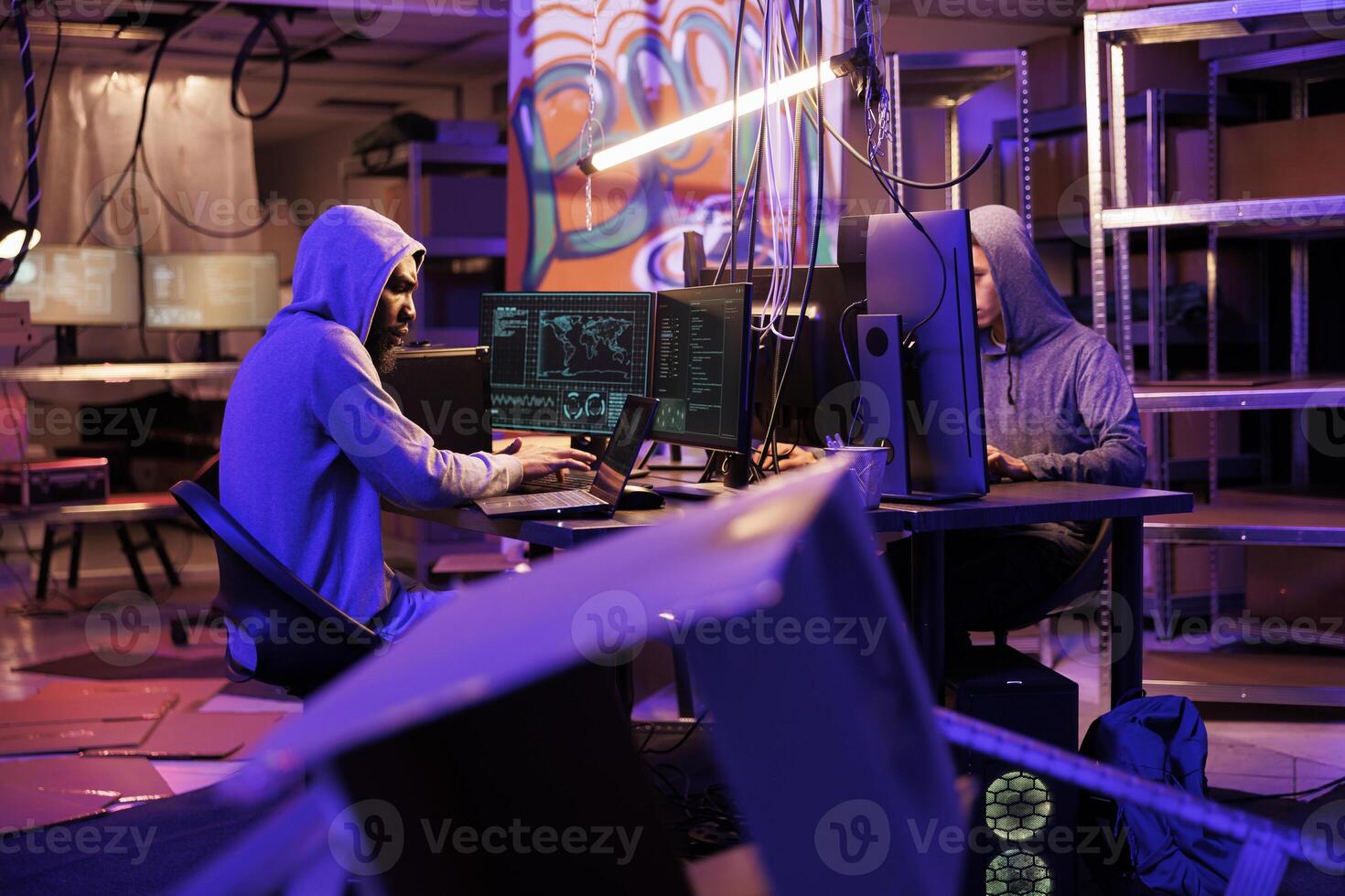 Hacker group collaborating in abandoned warehouse while hacking government server on computer. Criminals working together while coding internet virus software for data breach photo