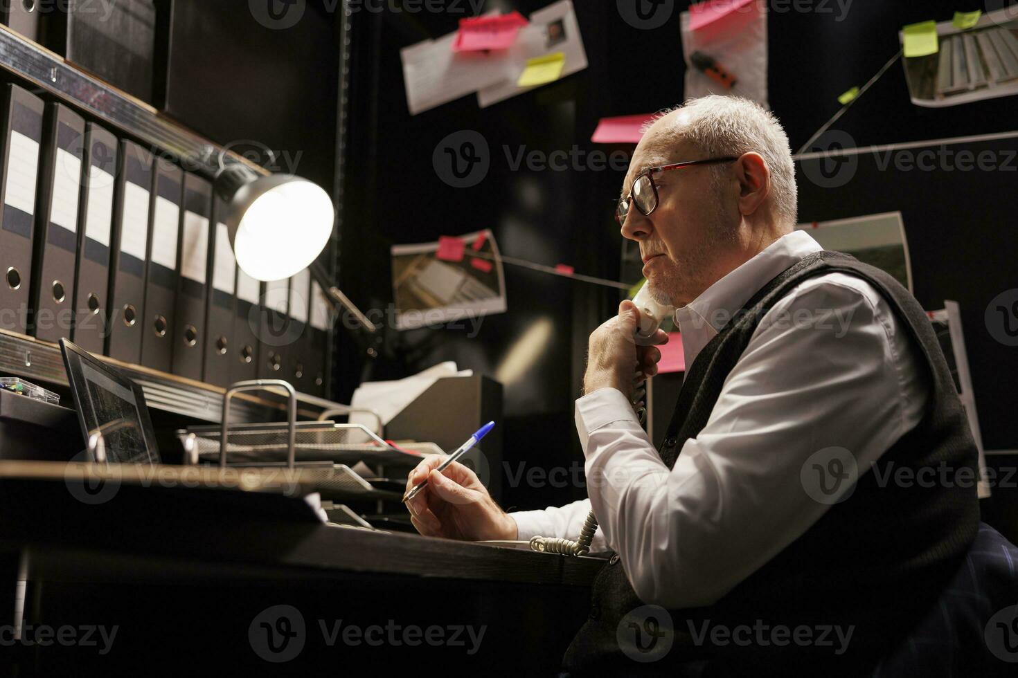 Investigator having remote conversation with police officer, discussing crime scene report using landline phone. Old detective working overhours at mysterious criminal case, analyzing crime evidence photo