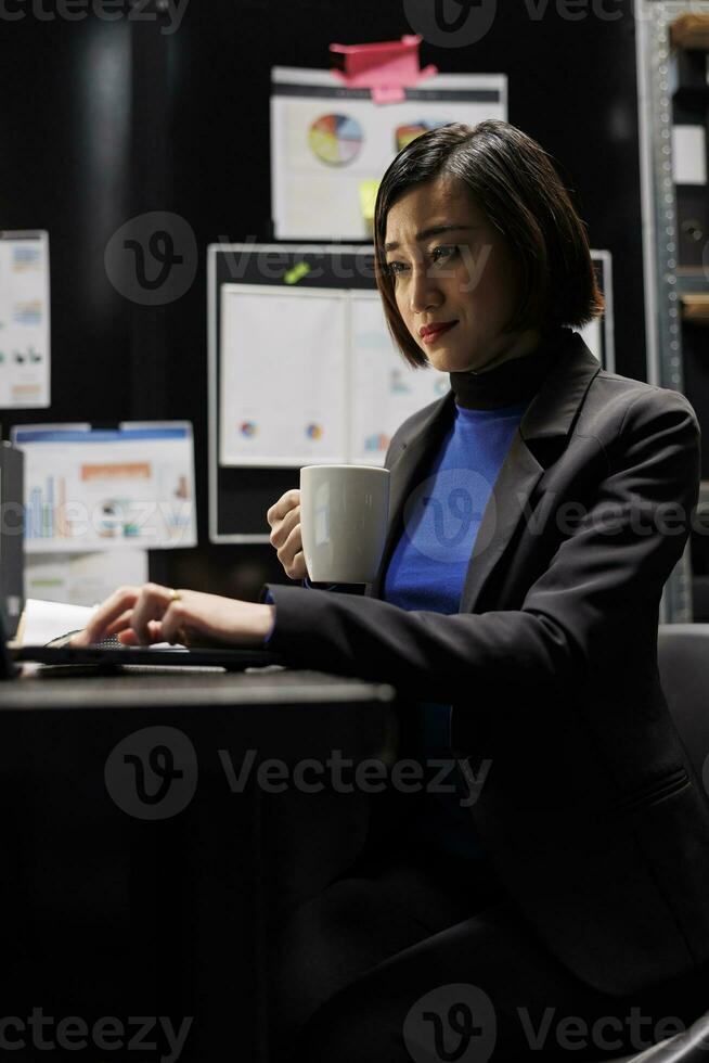 Accountant businesswoman manager enjoying mug of coffee starting her shift in business administration workplace. Asian executive sitting at office desk before consulting meeting photo