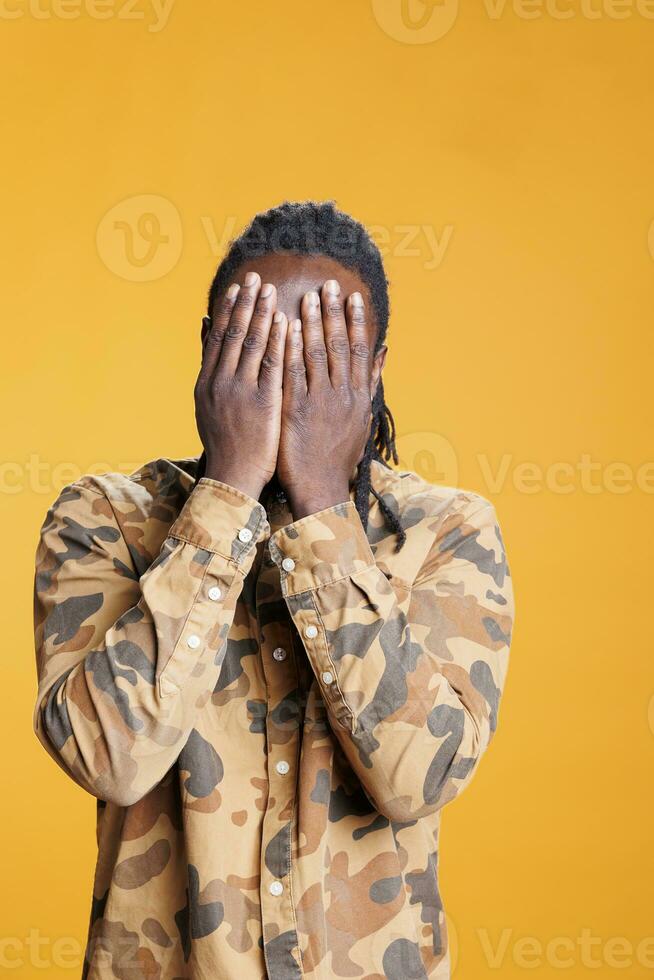 Male person doing three wise monkeys gesture on camera, covering eyes, mouth and ears as wisdom sayings. African american man advertising silence concept with hand in studio over background photo