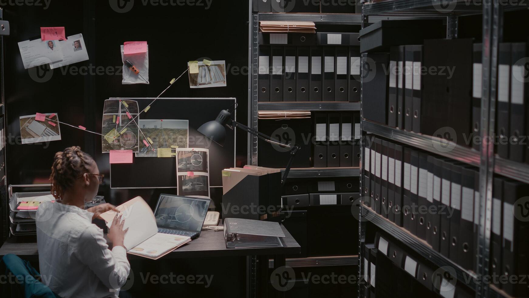 Law enforcement agent reading archive records at desk, conducting investigation files in evidence room. Private investigator examining surveillance photos and materials, suspicious clues.