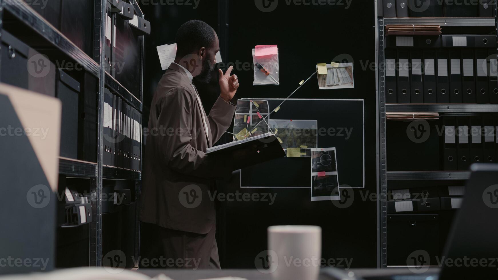 Police officer analyzing detective board with evidence, trying to solve crime or felony. Law agent doing detective work and catch suspect, using case files for investigation research. Handheld shot. photo