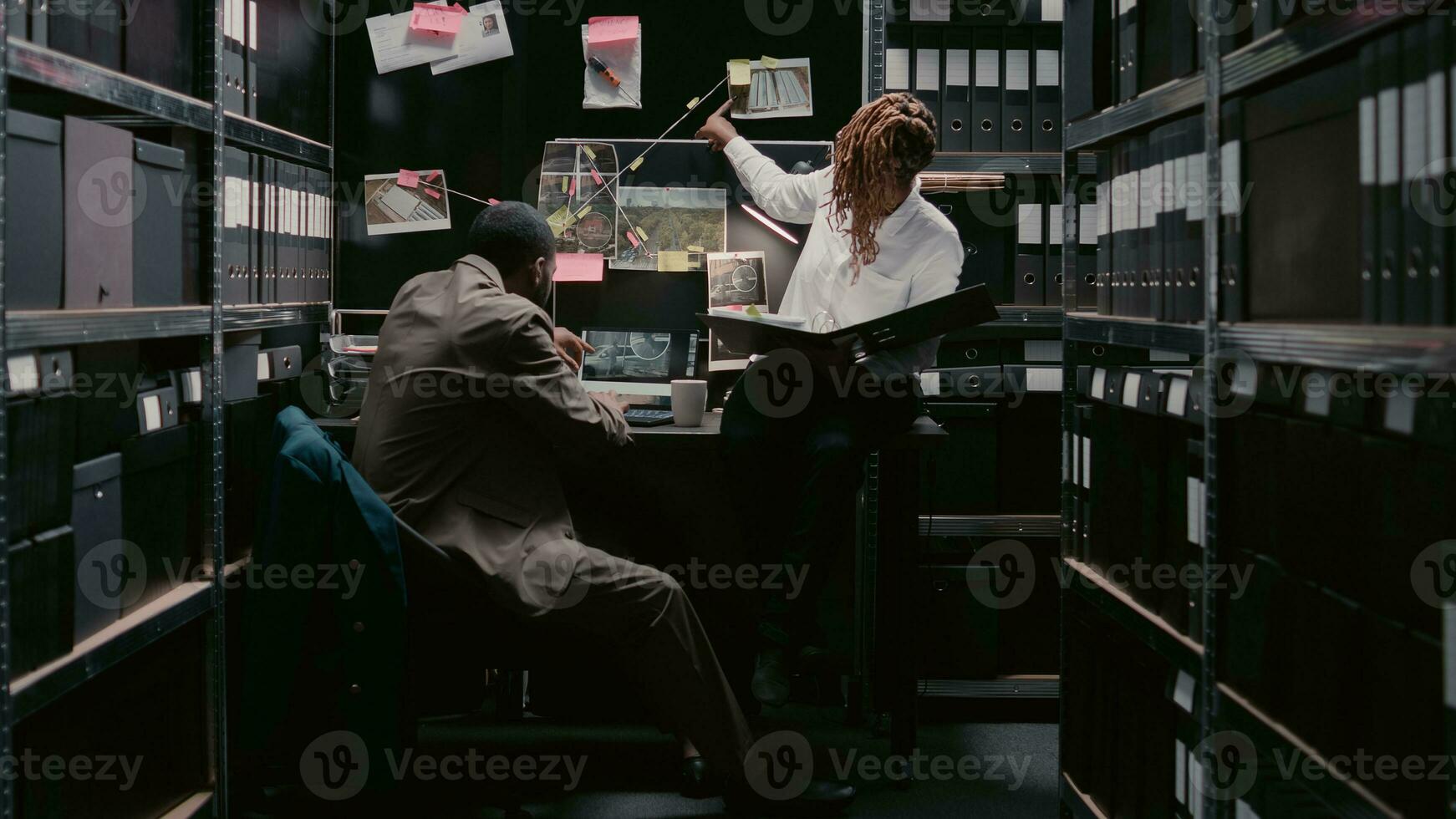 Two police officers examining case files reports, working on criminal investigation to catch suspect. Team of private detectives reading statements in archive room, looking at evidence map. photo