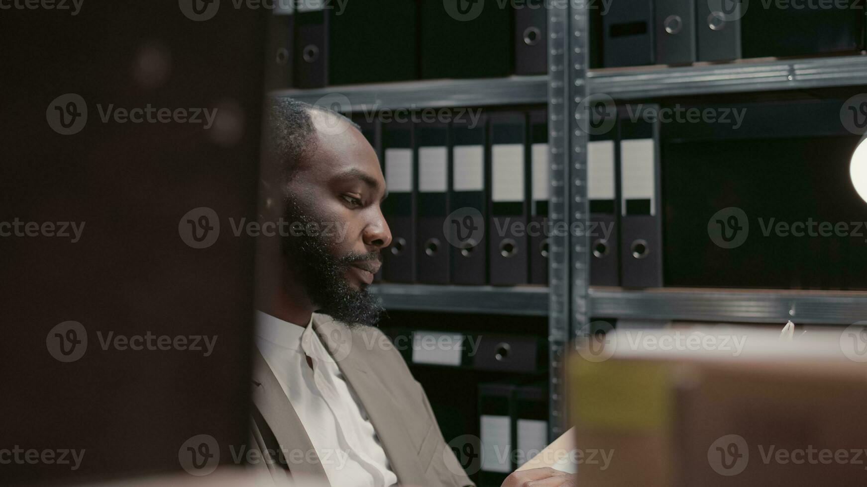 African american agent working on crime case with files, analyzing forensic evidence and documents in office space. Private detective conducting professional investigation. Tripod shot. photo