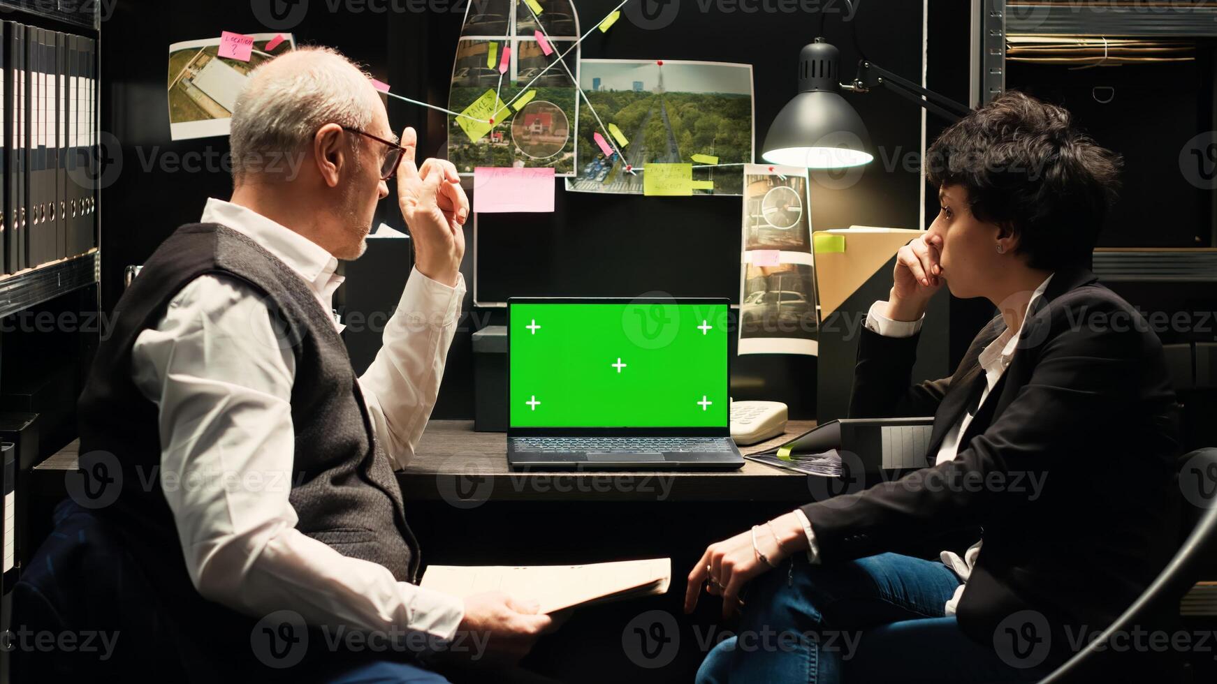 Police team using greenscreen display, working on criminal investigation. Two law agents reviewing isolated copyspace on laptop and reading witness statements for clues, detective work. photo