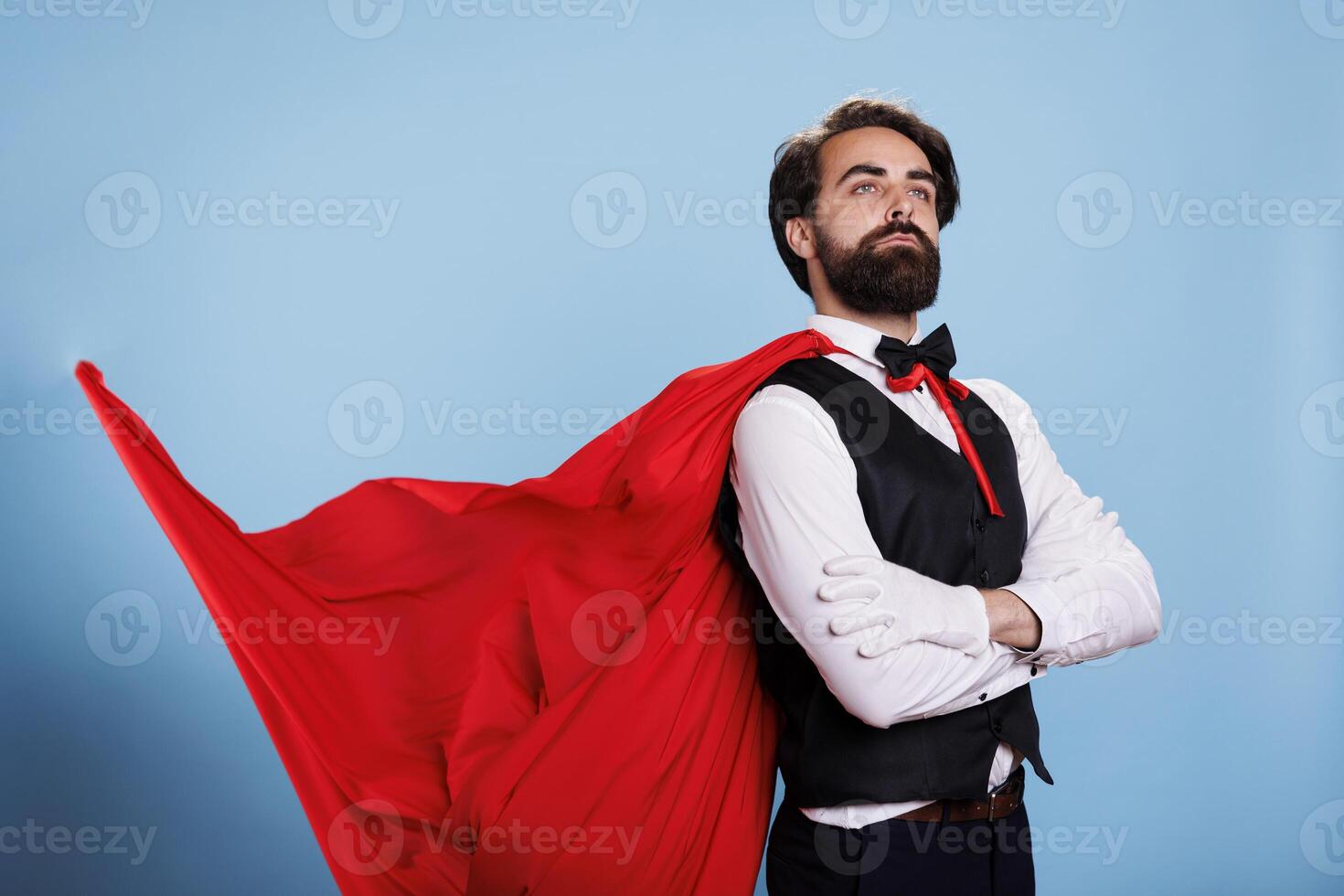 Powerful superhero wears red cape and feeling strong to save citizens, posing against blue background. Determined leader in formal clothes acting confident, fantasy cartoon concept. photo