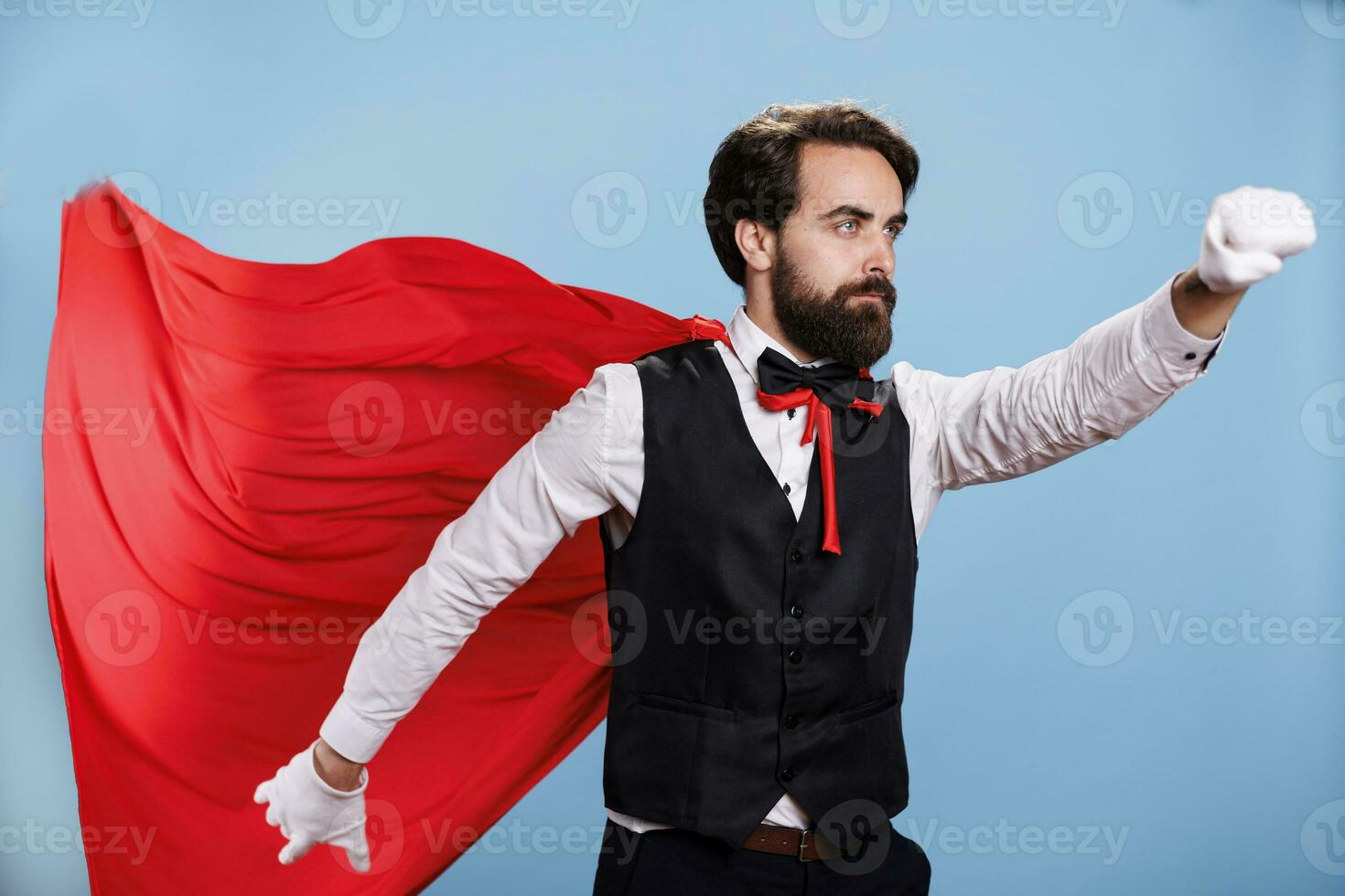 Professional person wears red cape in front of camera, posing with cartoon mantle for strength and force. Powerful man feeling strong while he wears fantasy costume as superhero. photo