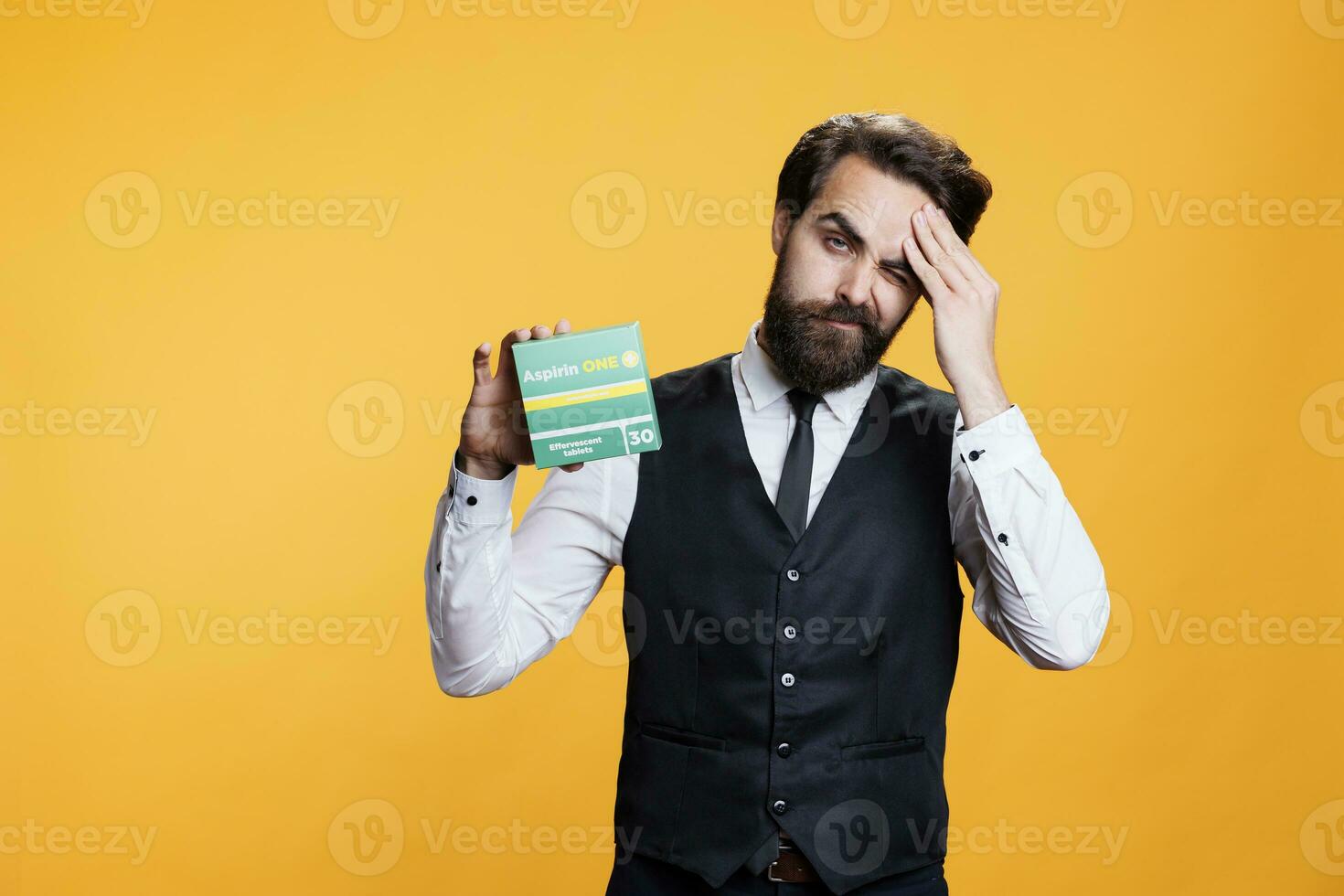 Professional waiter with headache recommends pills on camera, presenting box of painkillers to ease migraine or pain. Young adult feeling unwell and sick, holding medication package. photo