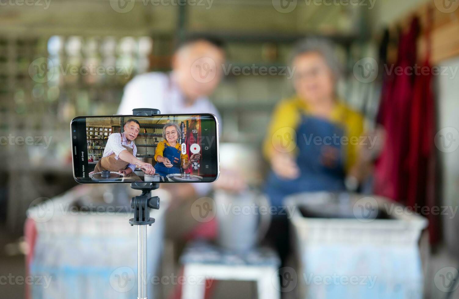 Asian retired couple with pottery making and clay painting activities in the pottery workshop with live broadcasting via social media channels photo