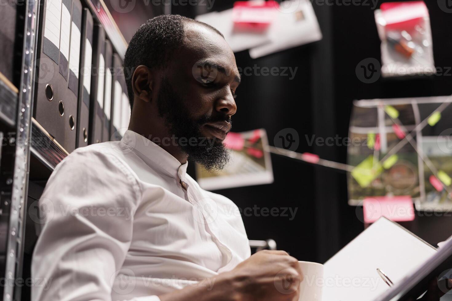 African american investigator reading police documentation, working late. Man detective studying folder with forensic expertise and conducting investigation to solve crime photo