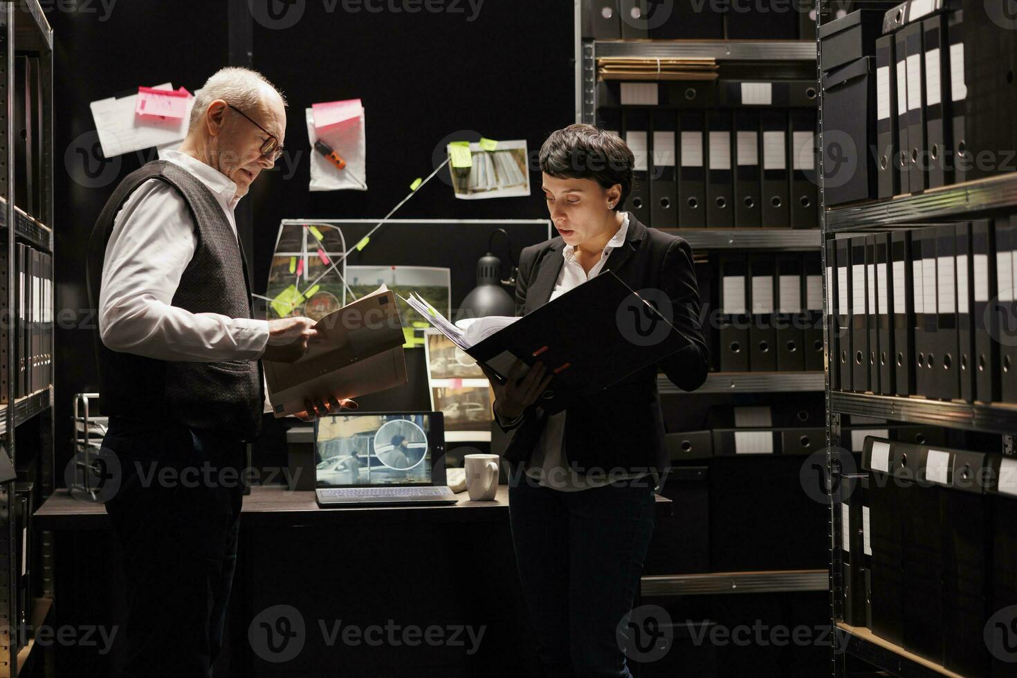 Police officers analyzing confidential federal files, working late at night at mysterious criminal case in arhive room. Criminology team checking crime scene evidence, looking at victim report photo