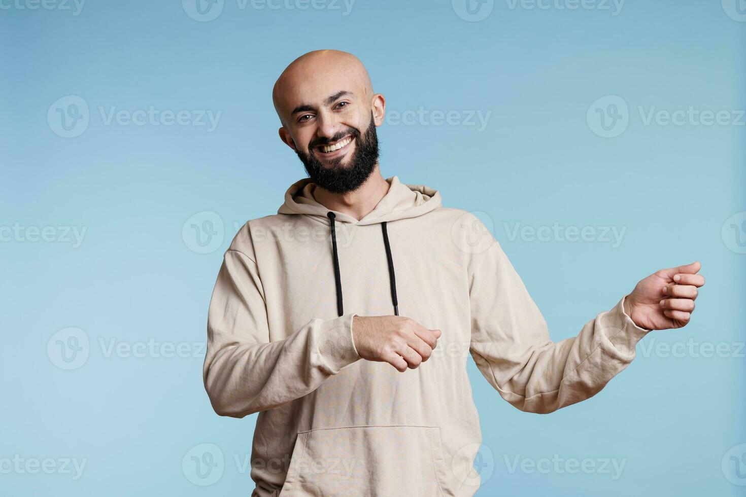 Cheerful arab man promoting product and holding invisible banner for ads portrait. Smiling person pretending to carry placard in two hands and looking at camera with happy expression photo