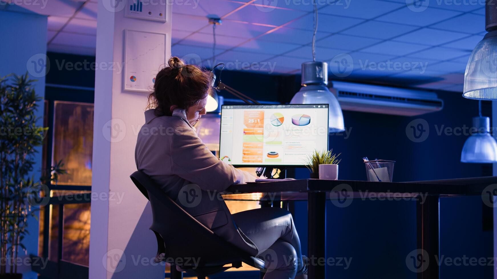 Female advisor answering landine phone call in office, using telephone line to have remote chat at night. Professional manager planning business report for company development. photo