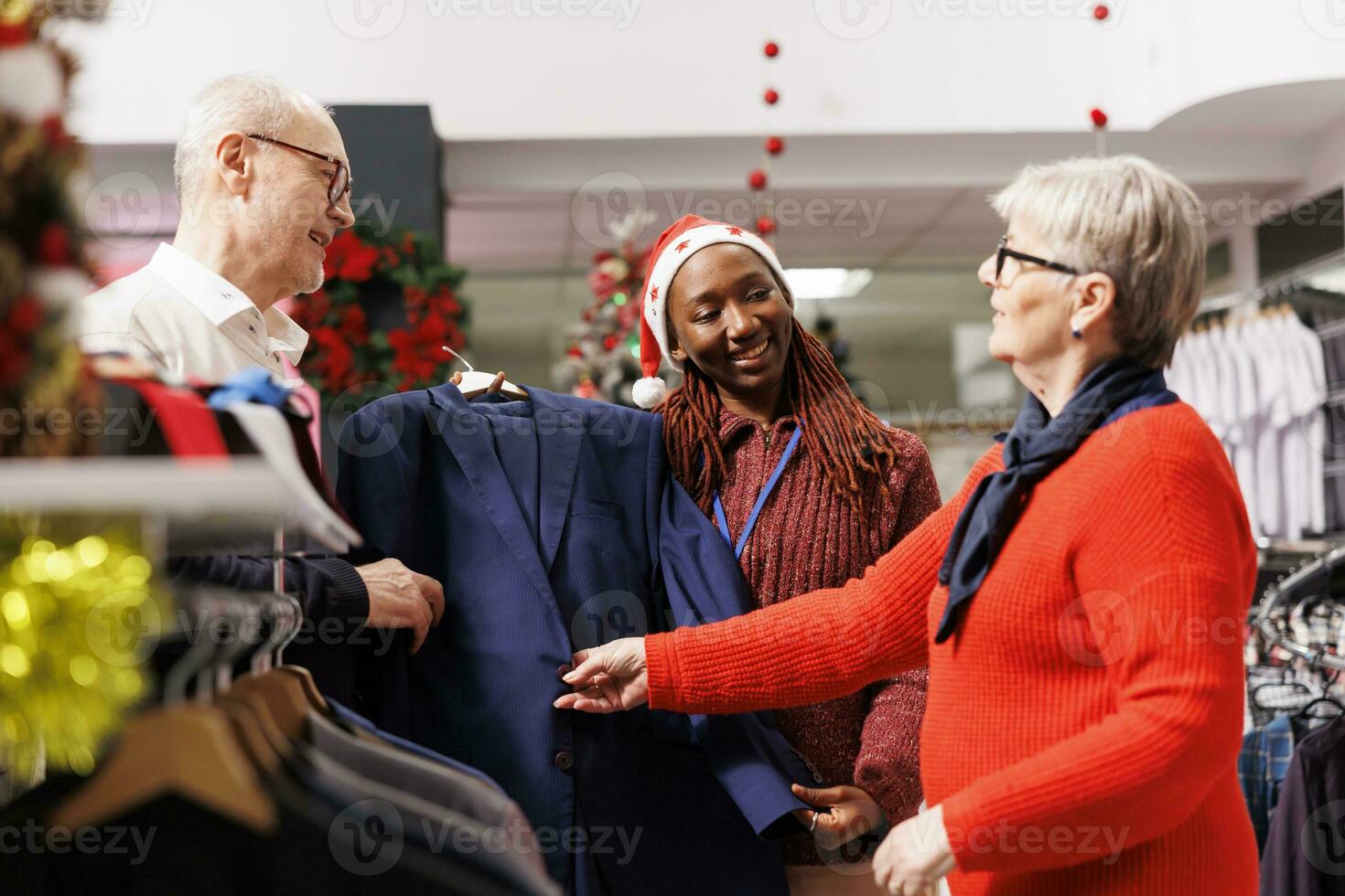 Sales assistant holding suit jacket for senior people, recommending perfect clothes for christmas eve outfit. Woman store employee helping clients buy formal attire, presenting merchandise. photo