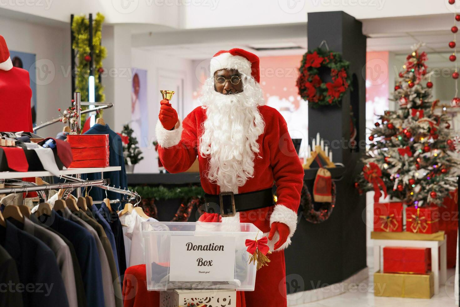 Santa claus ringing bell to call for customers next donation box, encouraging people to give clothes away to charity during winter holidays. Employee working on donating goods the poor. photo