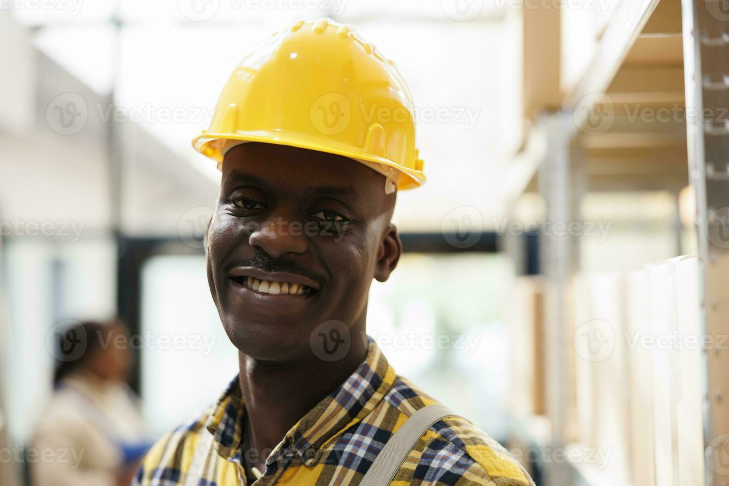 African american warehouse package handler in yellow helmet portrait. Industrial storehouse young loader wearing protective workwear smiling and looking at camera close up photo