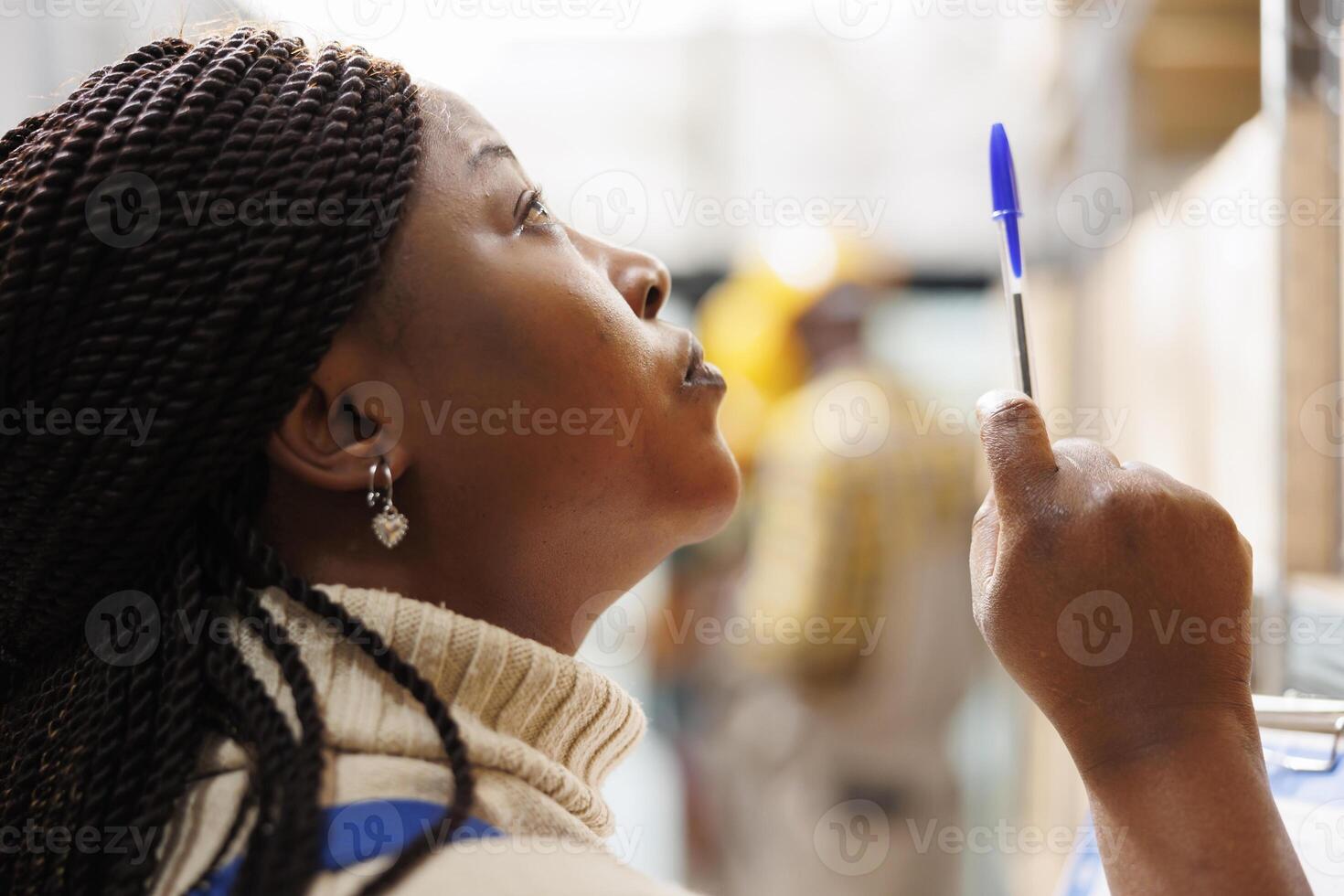 African american warehouse manager looking upwards and pointing with pen. Storehouse woman supervisor maintaining documentation and checking parcels storage face close up photo